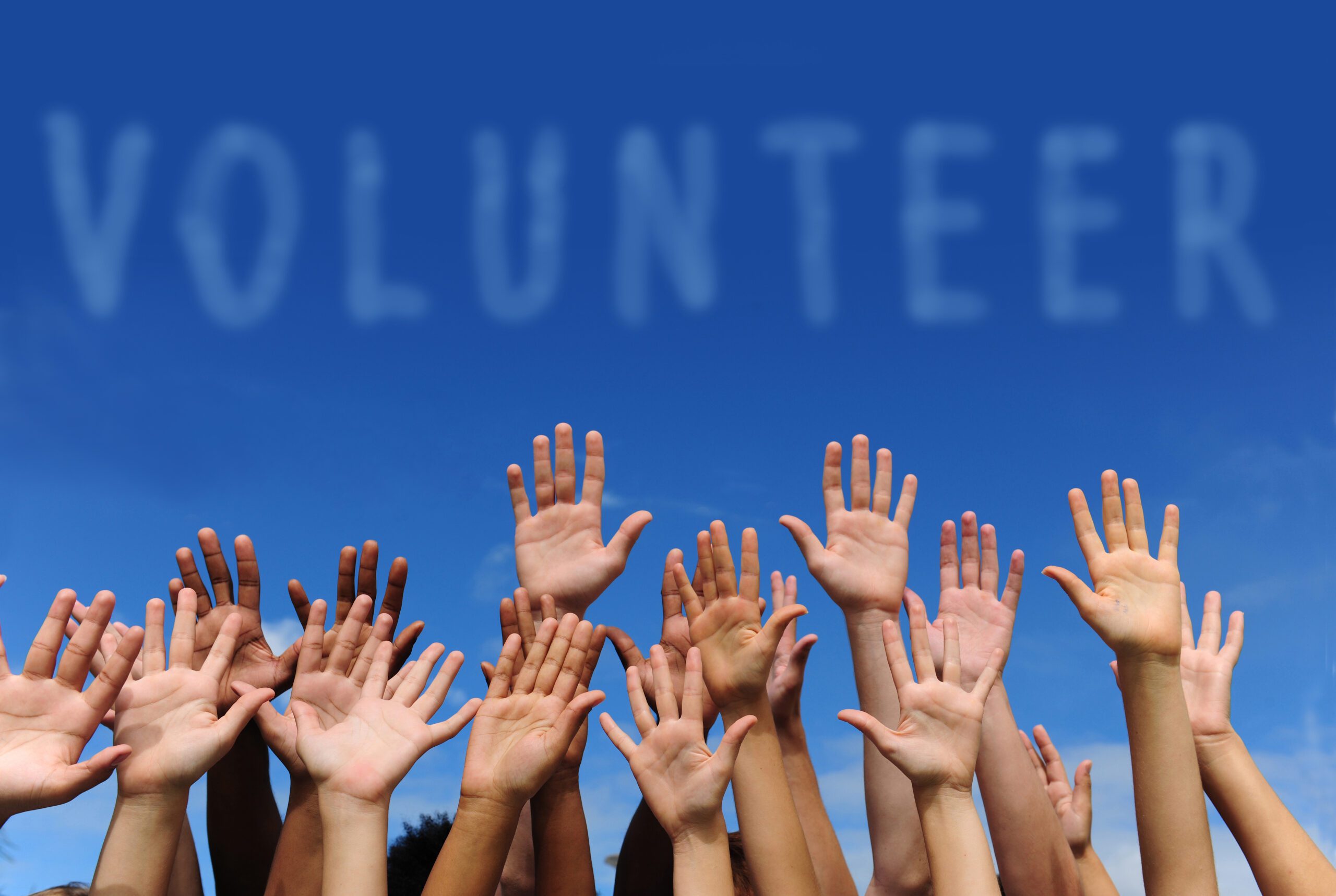 Volunteer,Group,Raising,Hands,Against,Blue,Sky,Background